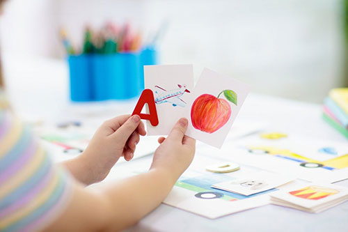 A child holding some flash cards showing the letter A, an aeroplane, and an apple